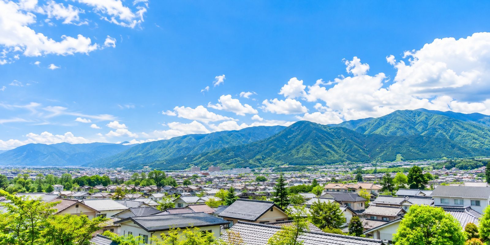 晴れた日の長野の住宅街と、奥に広がる緑の山並み(イメージ)